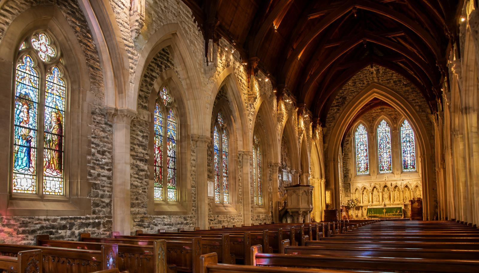 Stained glass and wooden pews inside a historic stone church sanctuary