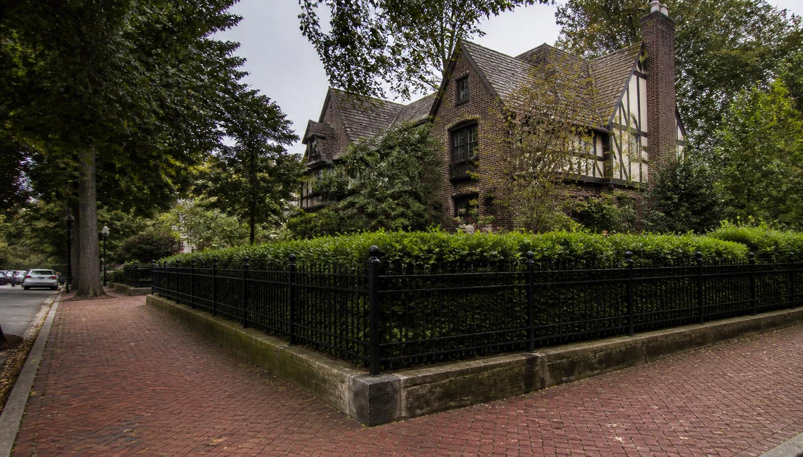 Brick Tudor Revival home behind a wrought-iron fence on a brick-paved corner
